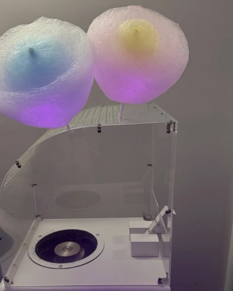 Two large clouds of freshly spun fairy floss on sticks resting on the Flossed Fairy machine